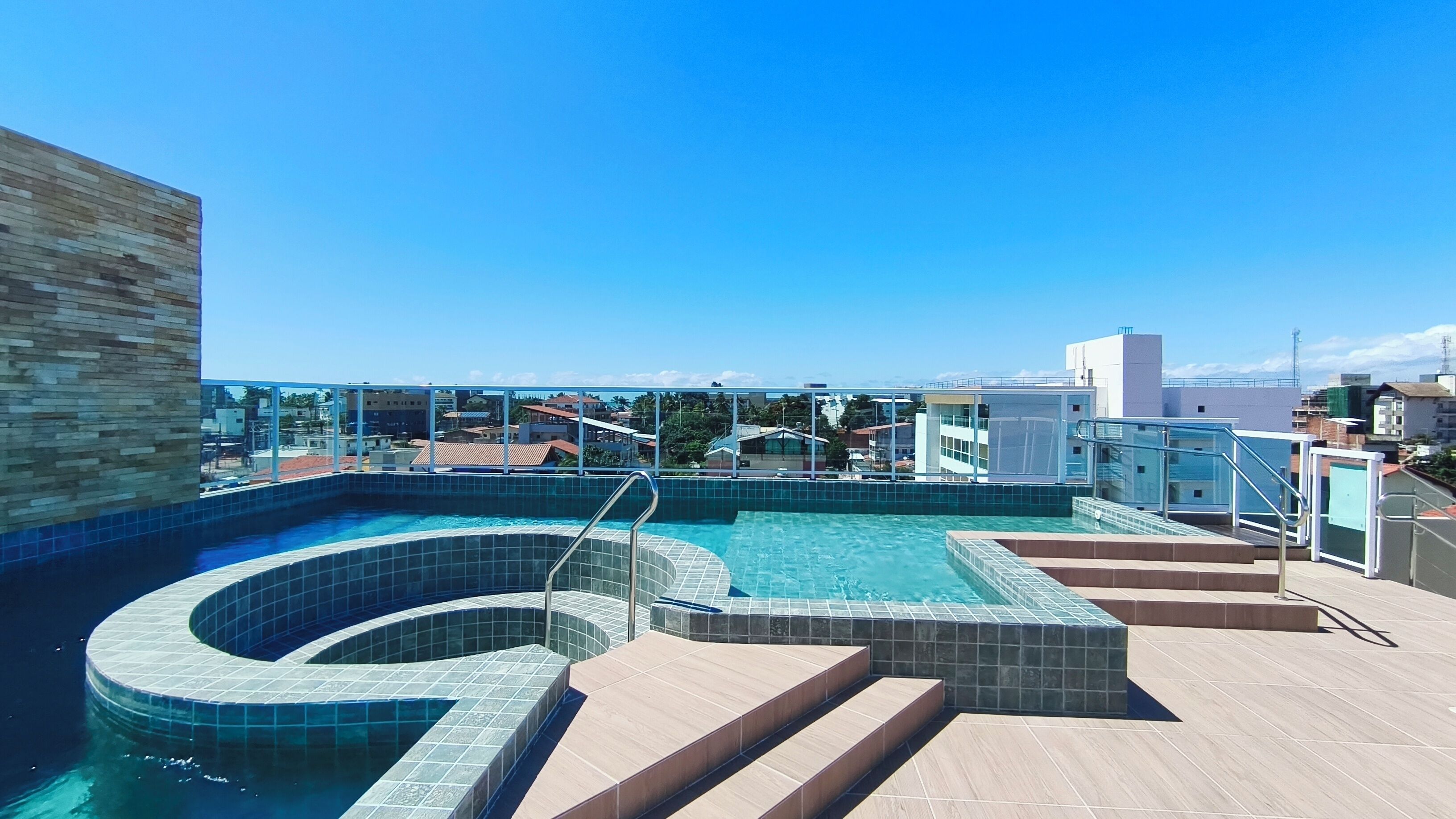 Uma piscina no terraço com design curvo, rodeada por um deck ladrilhado e um guarda-corpo de vidro.