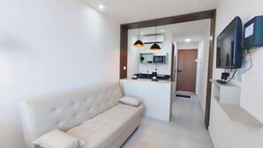 Una sala de estar moderna con un sofá, una zona de cocina con microondas y un televisor montado en la pared.