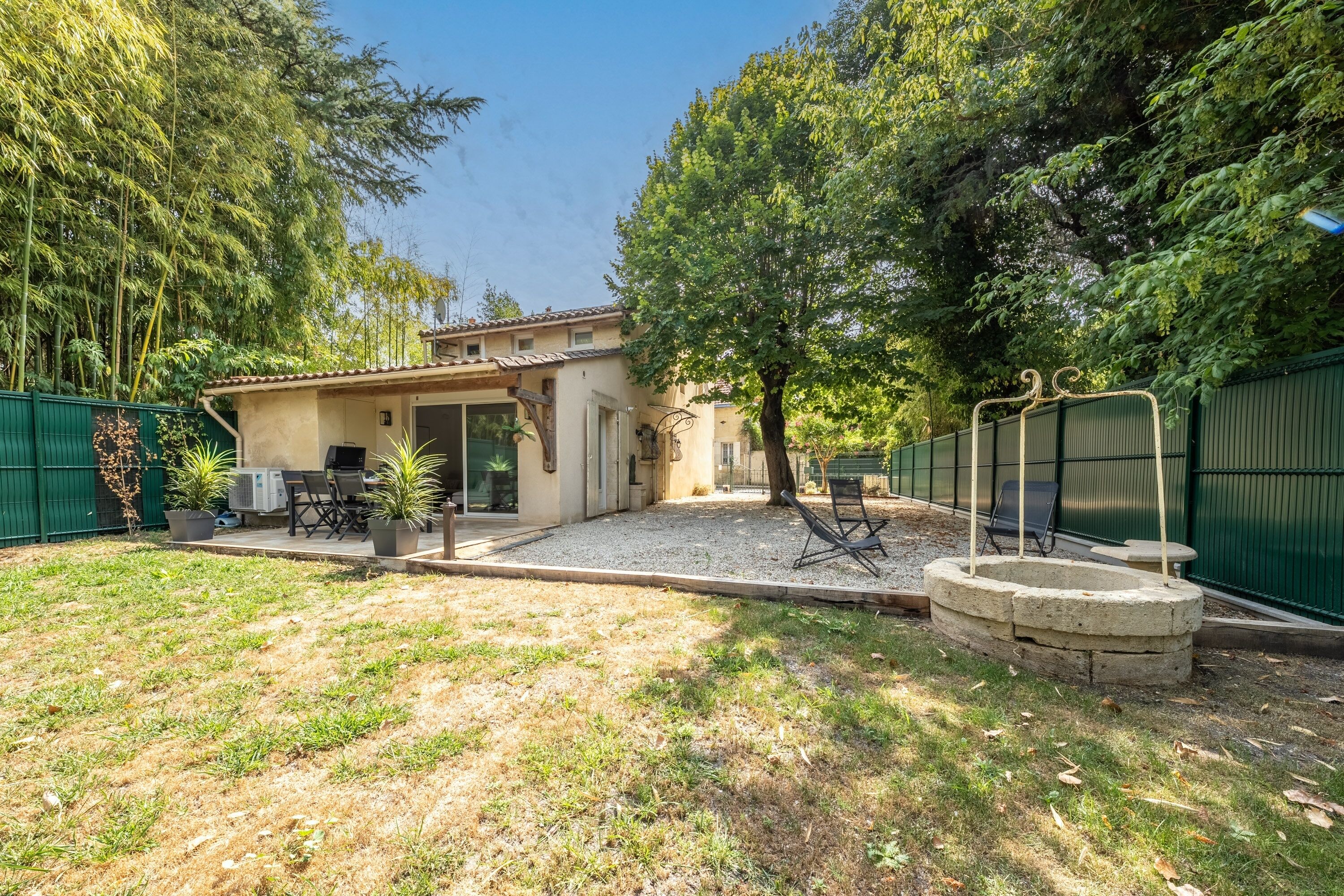 Une maison avec un patio, un foyer extérieur et une clôture verte.