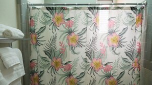 Casa de banho com cortina de chuveiro estampada com flores, toalheiro com toalhas dobradas e paredes revestidas a azulejos.