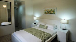 Quarto de hotel com uma cama, duas mesas de cabeceira com luminárias, um espelho e um quadro na parede.