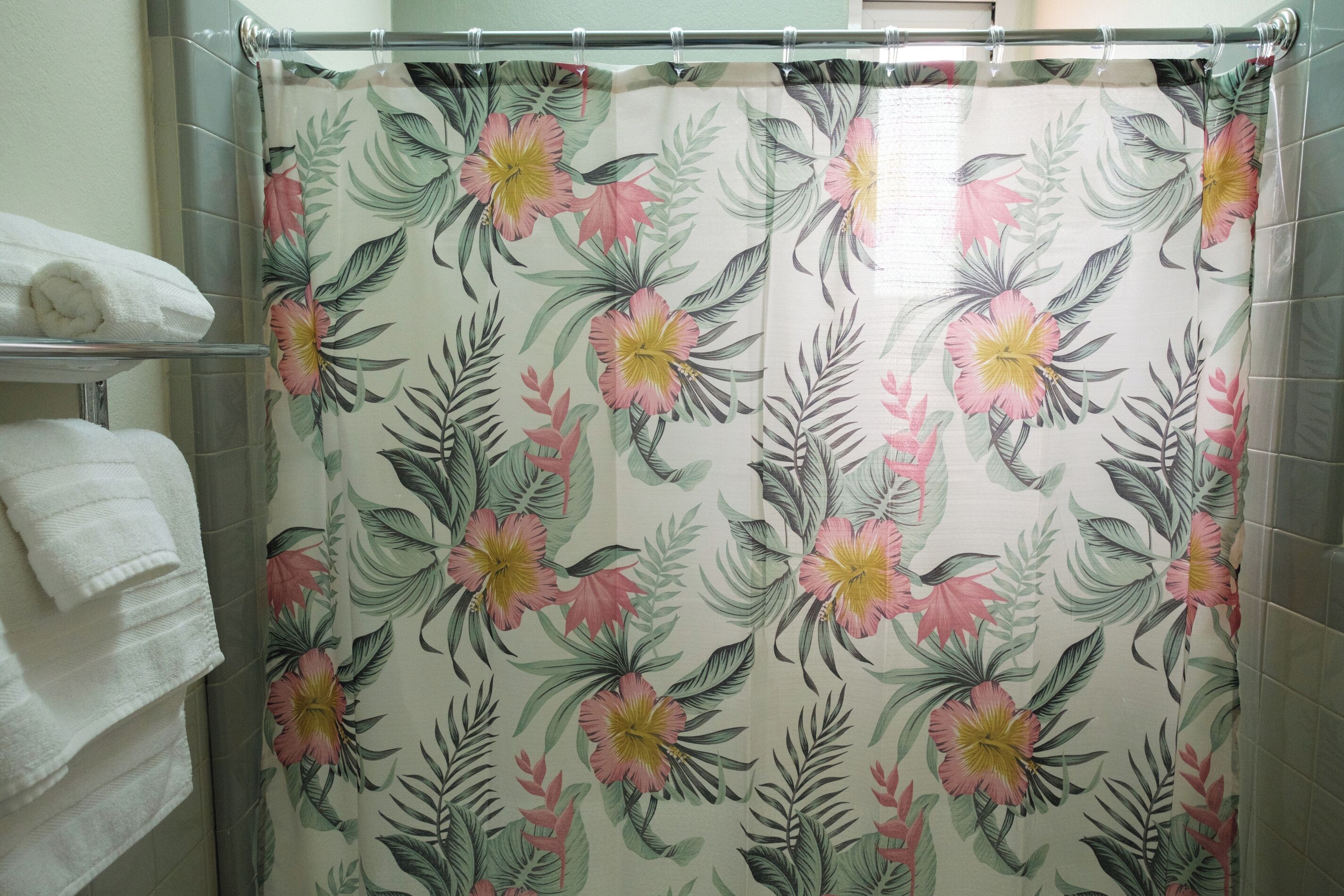 A bathroom with a shower curtain featuring a floral pattern, a towel rack with folded towels, and tiled walls.