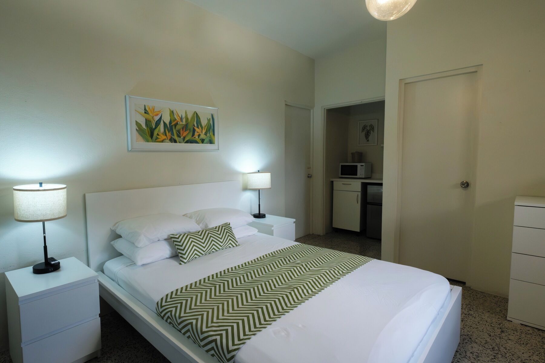 Hotelkamer met een bed, twee nachtkastjes, een lamp, een schilderij, een magnetron, een koelkast en een deur.