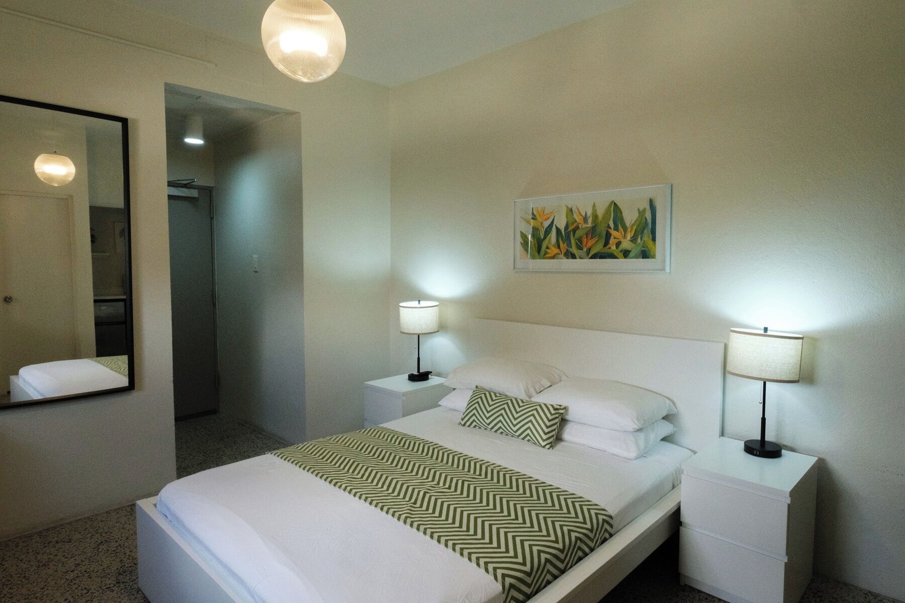 A hotel room with a bed, two bedside tables with lamps, a mirror, and a painting on the wall.