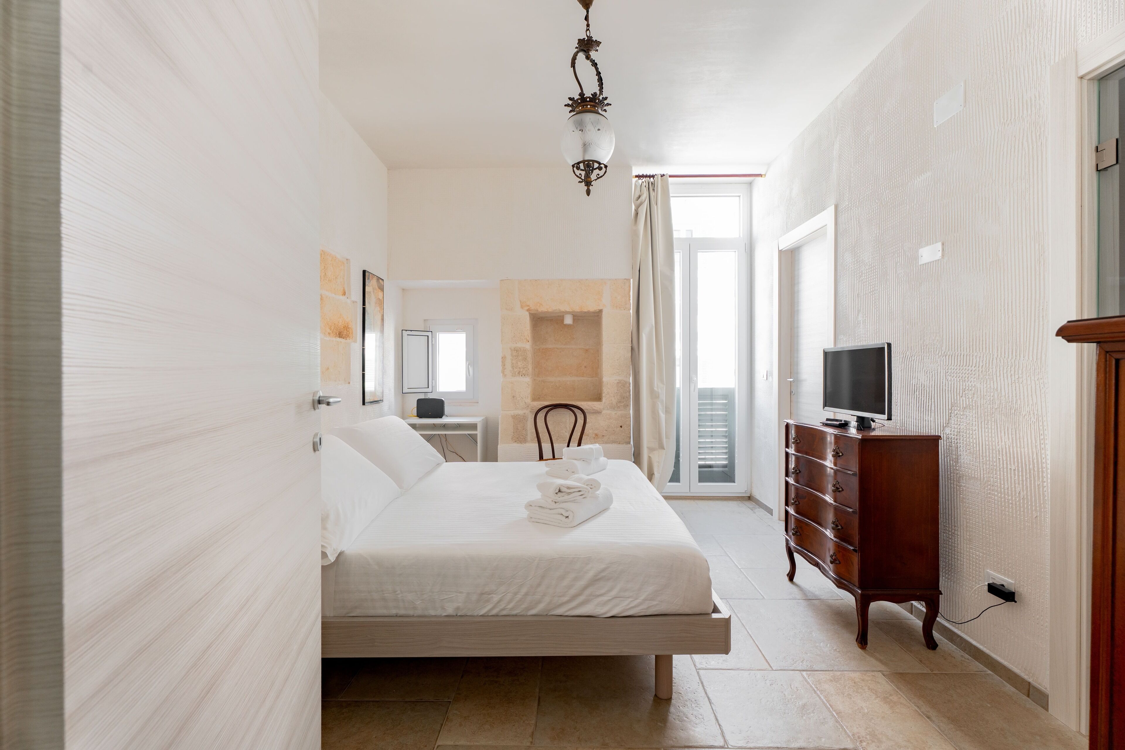 A bedroom with a bed, a dresser, a television, and a bathroom visible in the background.