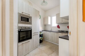 Una cocina con armarios de madera, microondas, horno, lavamanos y ventana.