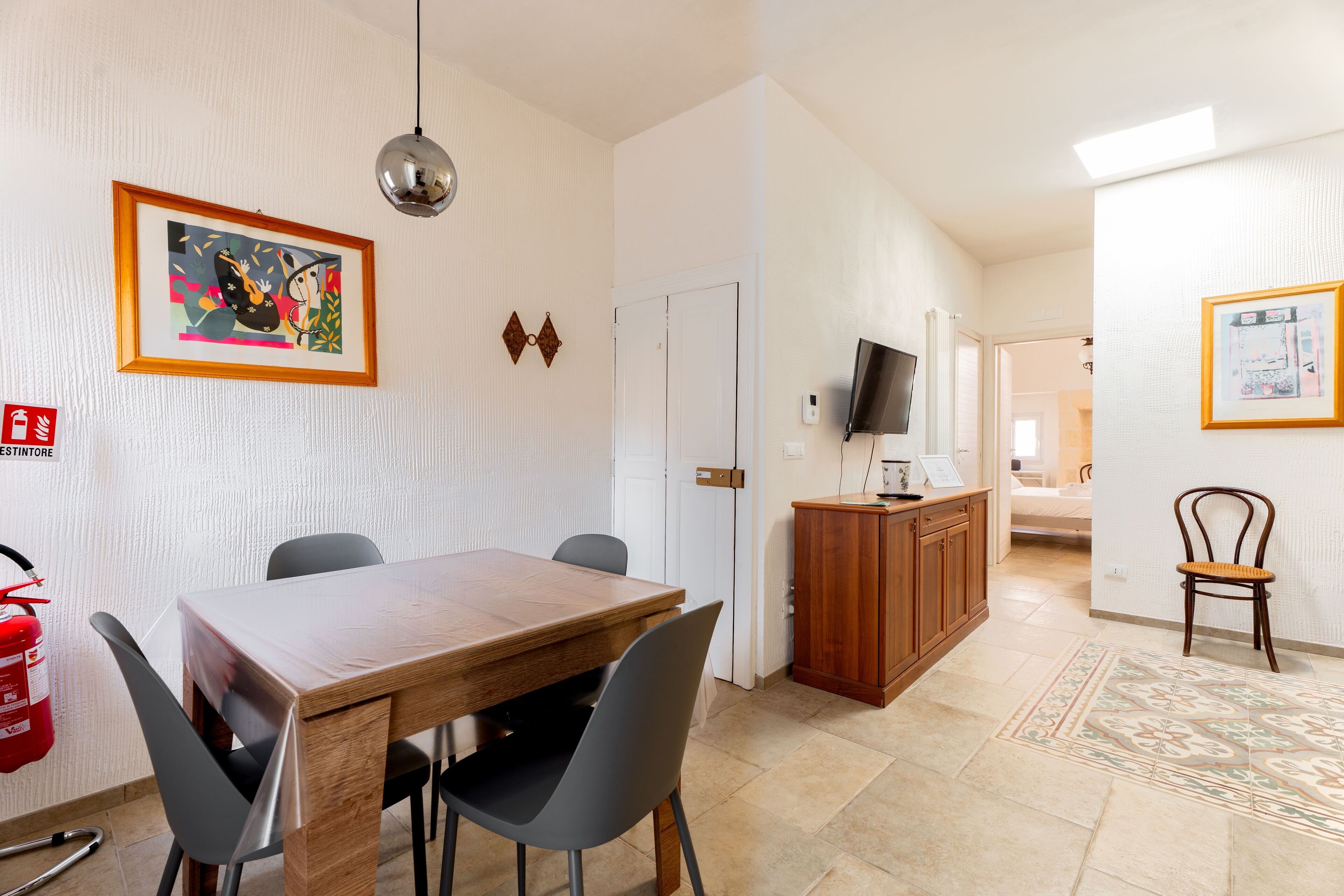 A dining area with a wooden table, four chairs, a fire extinguisher, a television, and a cabinet.