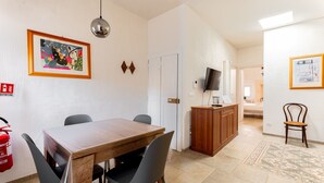 Ein Essbereich mit Holztisch, vier Stühlen, einem Feuerlöscher, einem Fernseher und einem Schrank.