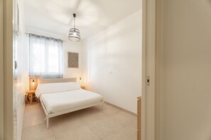 Un dormitorio con cama, lámparas de noche, una ventana con cortinas y un aplique de pared.