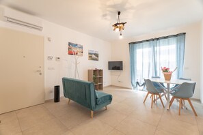 Una sala de estar con un sofá, una mesa de comedor con sillas, un televisor y una ventana con cortinas.