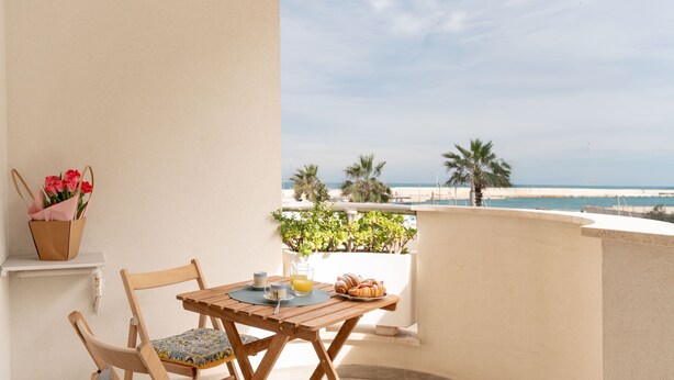 A balcony with a wooden table and chairs, a flower basket, and a breakfast setting with croissants and orange juice. - Alba di mare by Monholiday (Monopoli)