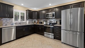 A modern kitchen with dark cabinets, stainless steel appliances, and a tiled backsplash. - Pelican's Cove (Port Orange)