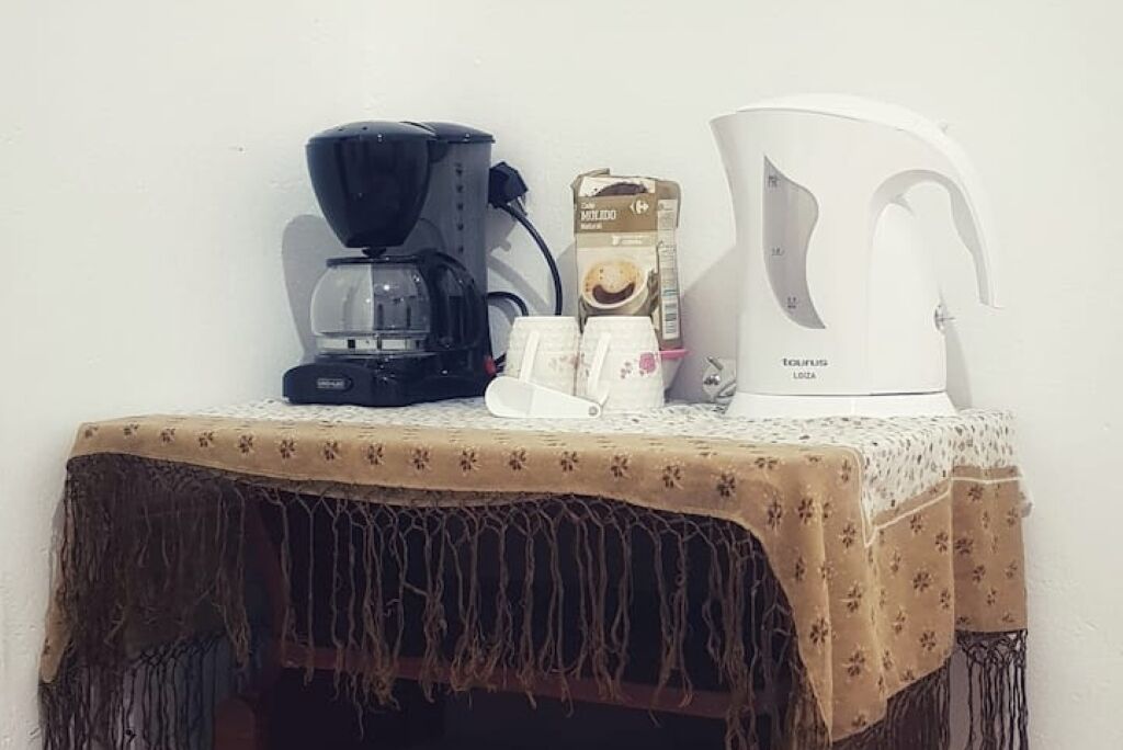 Una cafetera, un cartón de leche, una jarra de café y una taza sobre una mesa con mantel floreado.