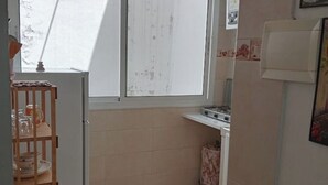 A compact kitchen with a window, a small stove, and a wooden shelf with dishes. - Studio Nahid 3rd floor free wifi (Tanger)