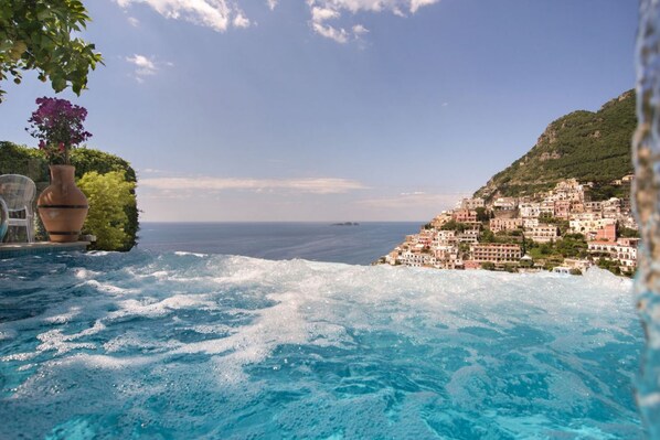 A view of a coastal town with buildings on a hillside, a clear sky, and a body of water in the foreground.