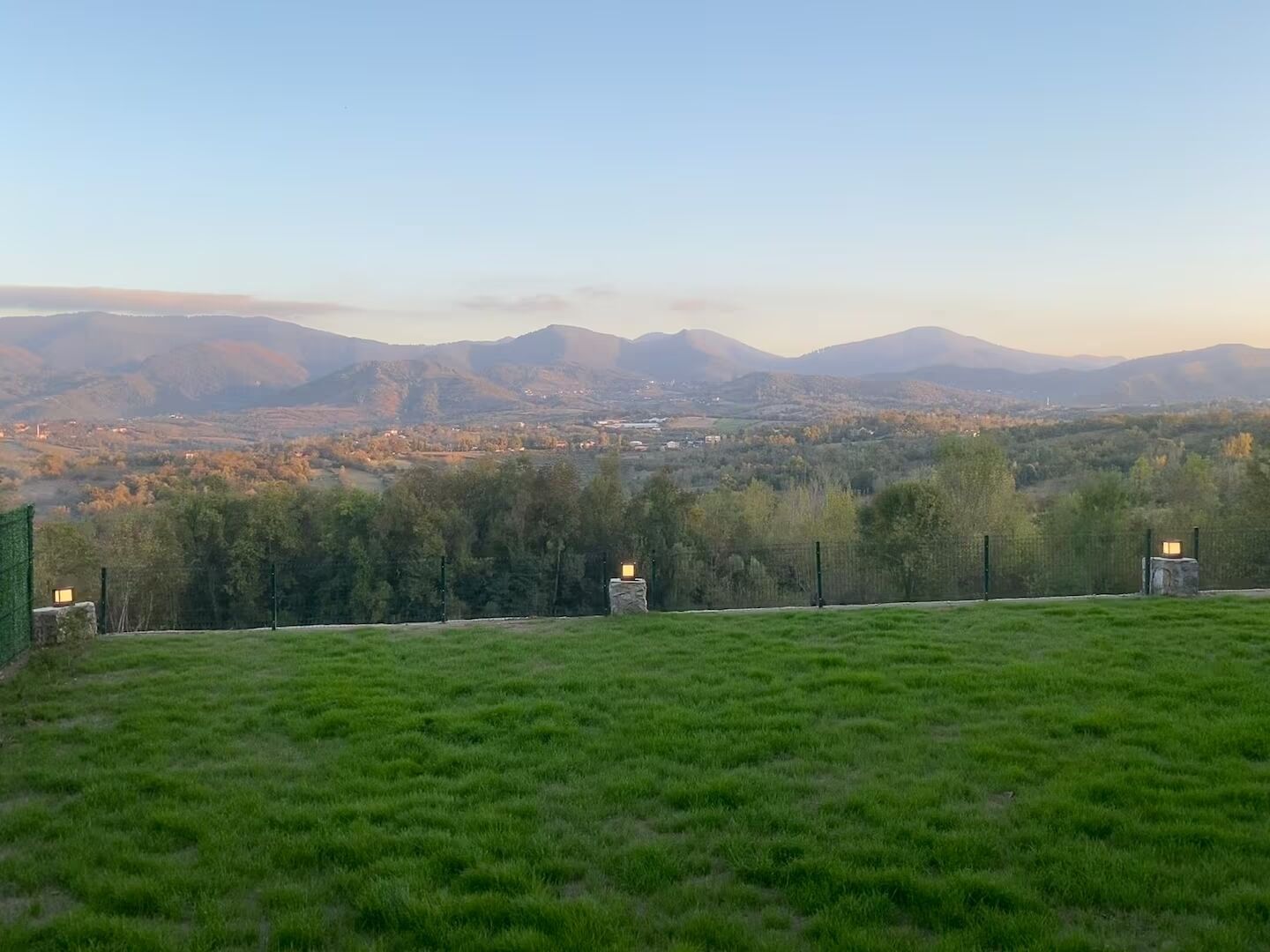 Un campo cubierto de césped con vistas a montañas lejanas y un pequeño asentamiento.
