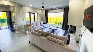 Amplio salón con un sofá grande, una mesa de centro y una chimenea. Hay un balcón con vistas a un campo amarillo.