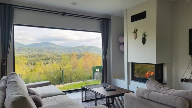 Una sala de estar moderna con un ventanal grande, una chimenea y vistas a un paisaje montañoso.