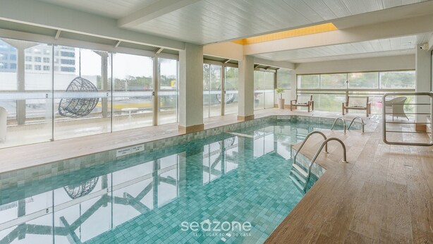 Ein Hallenbad mit großen Glaswänden, gefliestem Boden und Blick ins Freie.