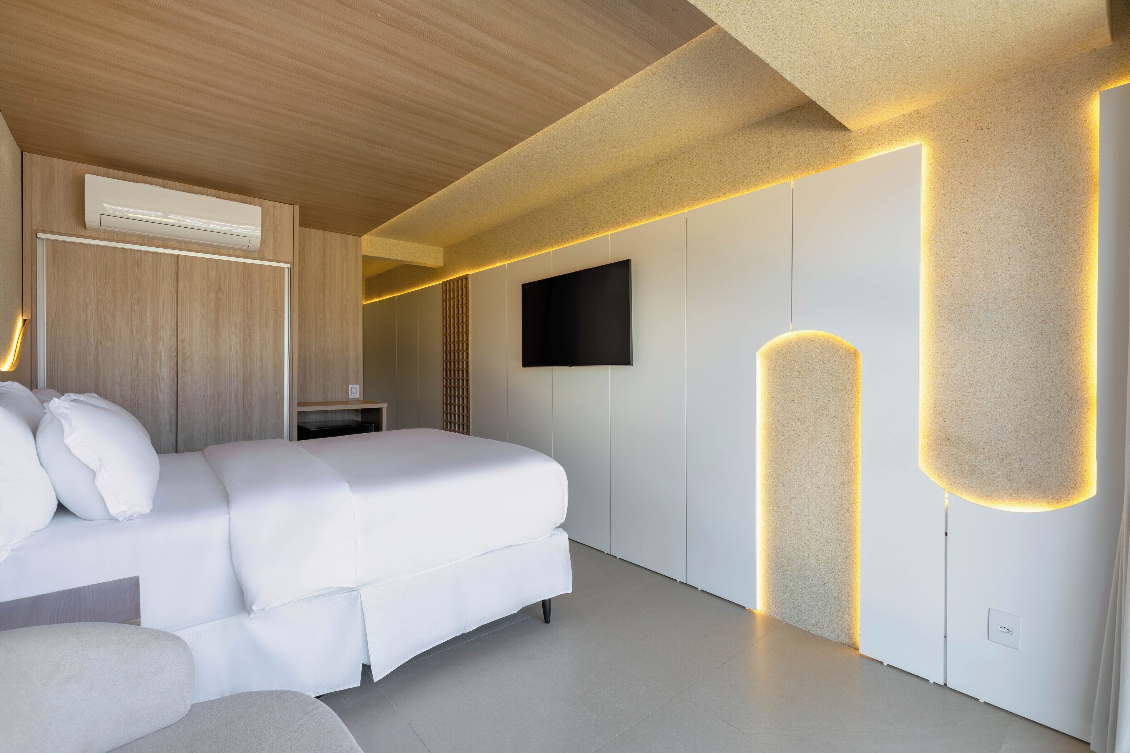 A modern bedroom with a large bed, a flat-screen TV, and ambient lighting.