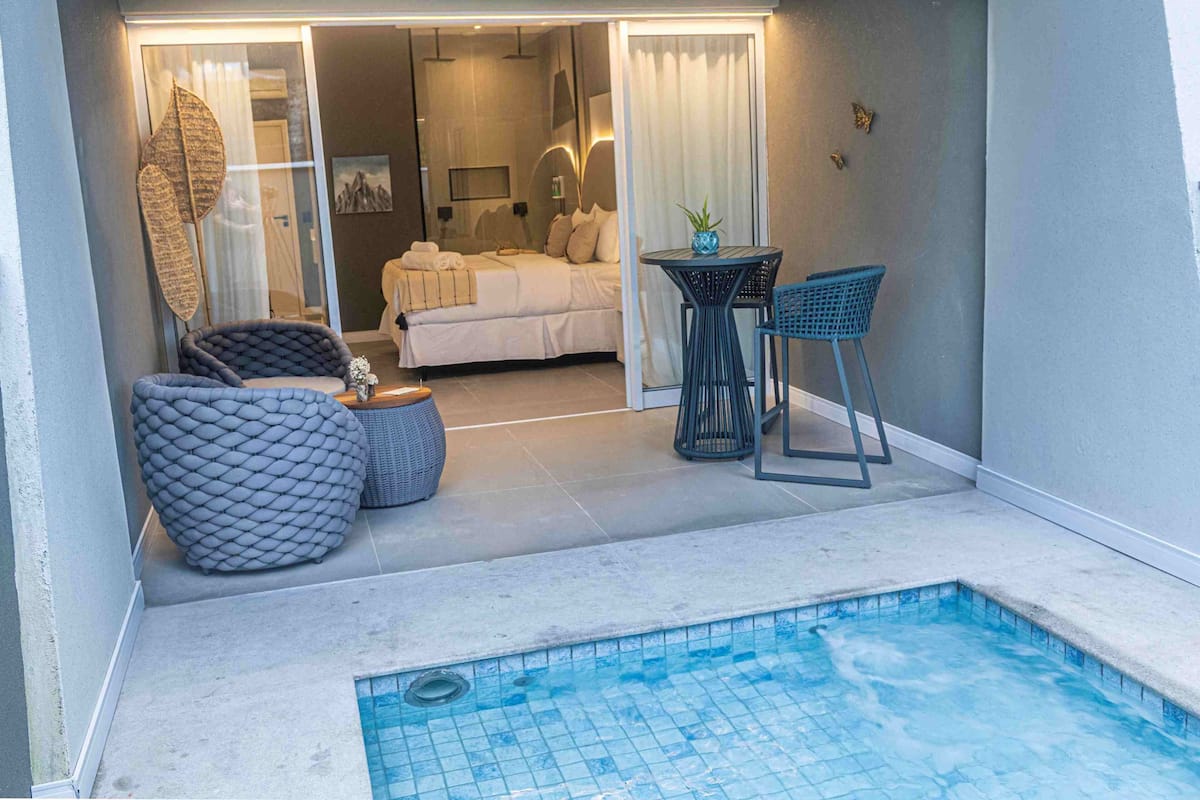 A hotel room with a bed, a small table with chairs, a pool, and a view of the interior.