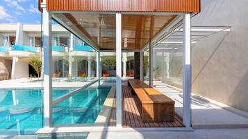 Un área de piscina moderna con un banco de madera y paredes de vidrio.