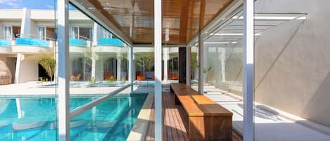 Un área de piscina moderna con un banco de madera y paredes de vidrio.