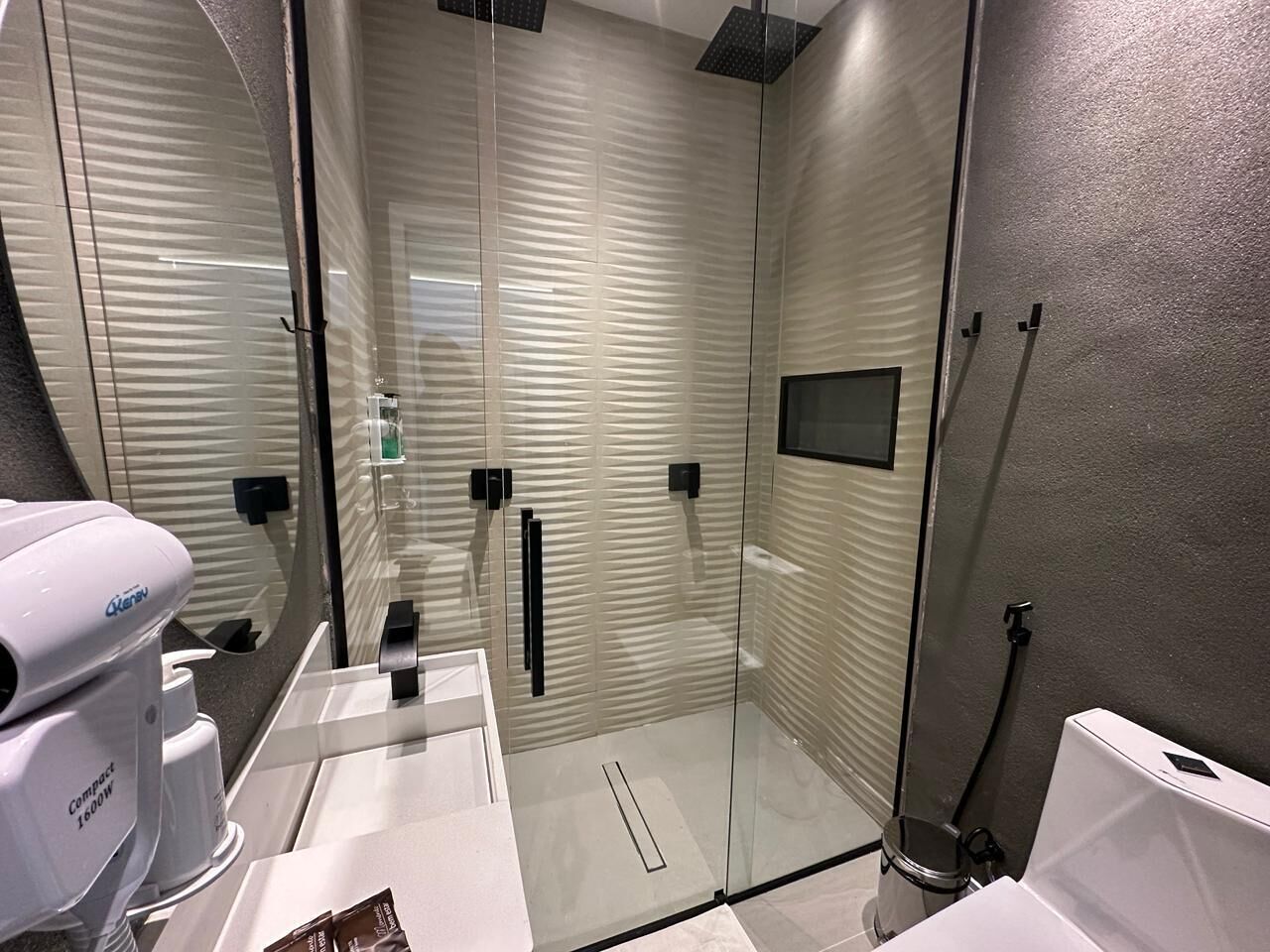 A modern bathroom with a glass shower enclosure, a compact coffee maker, and a toilet.
