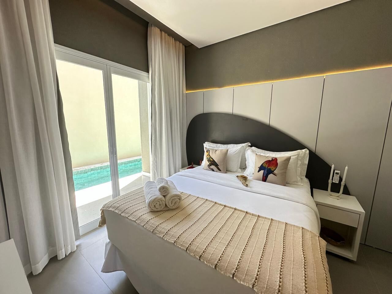 A modern hotel room with a large bed, a nightstand, and a view of the sea.