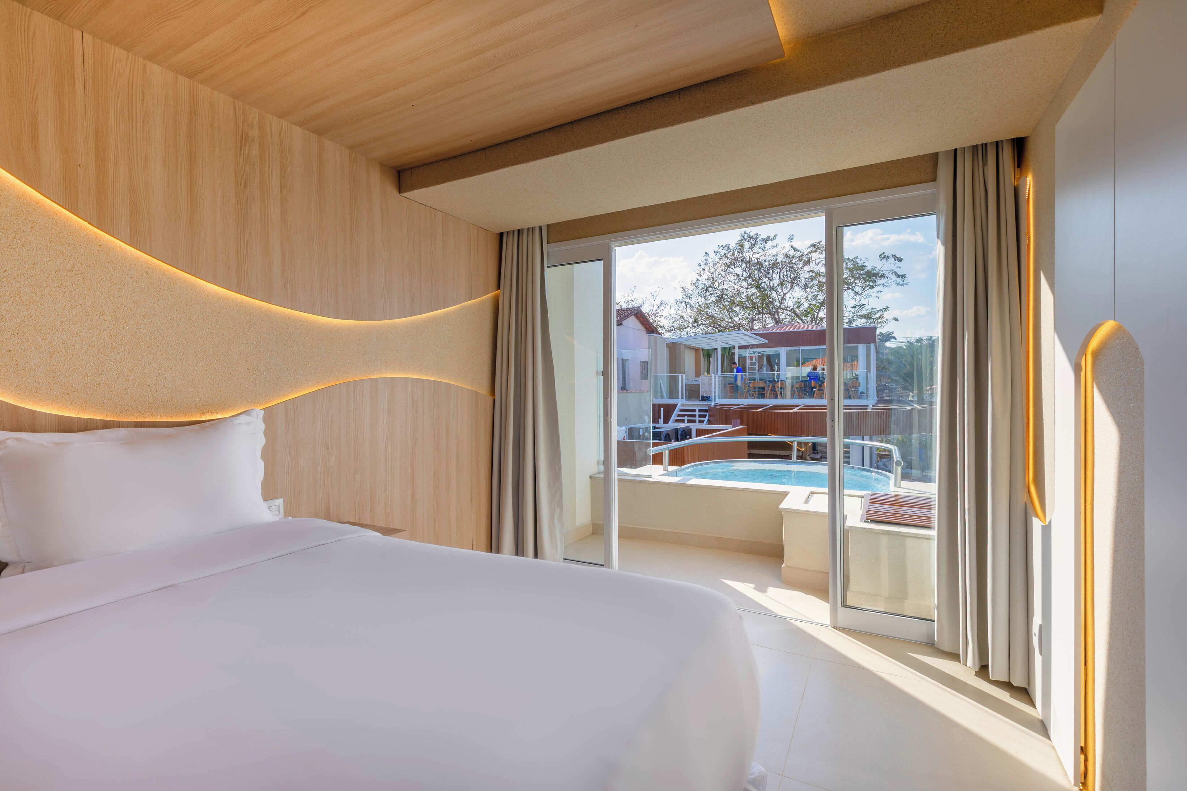 Ein modernes Hotelzimmer mit einem großen Bett, Blick auf einen Swimmingpool und einem Balkon mit Ausblick auf die Umgebung.