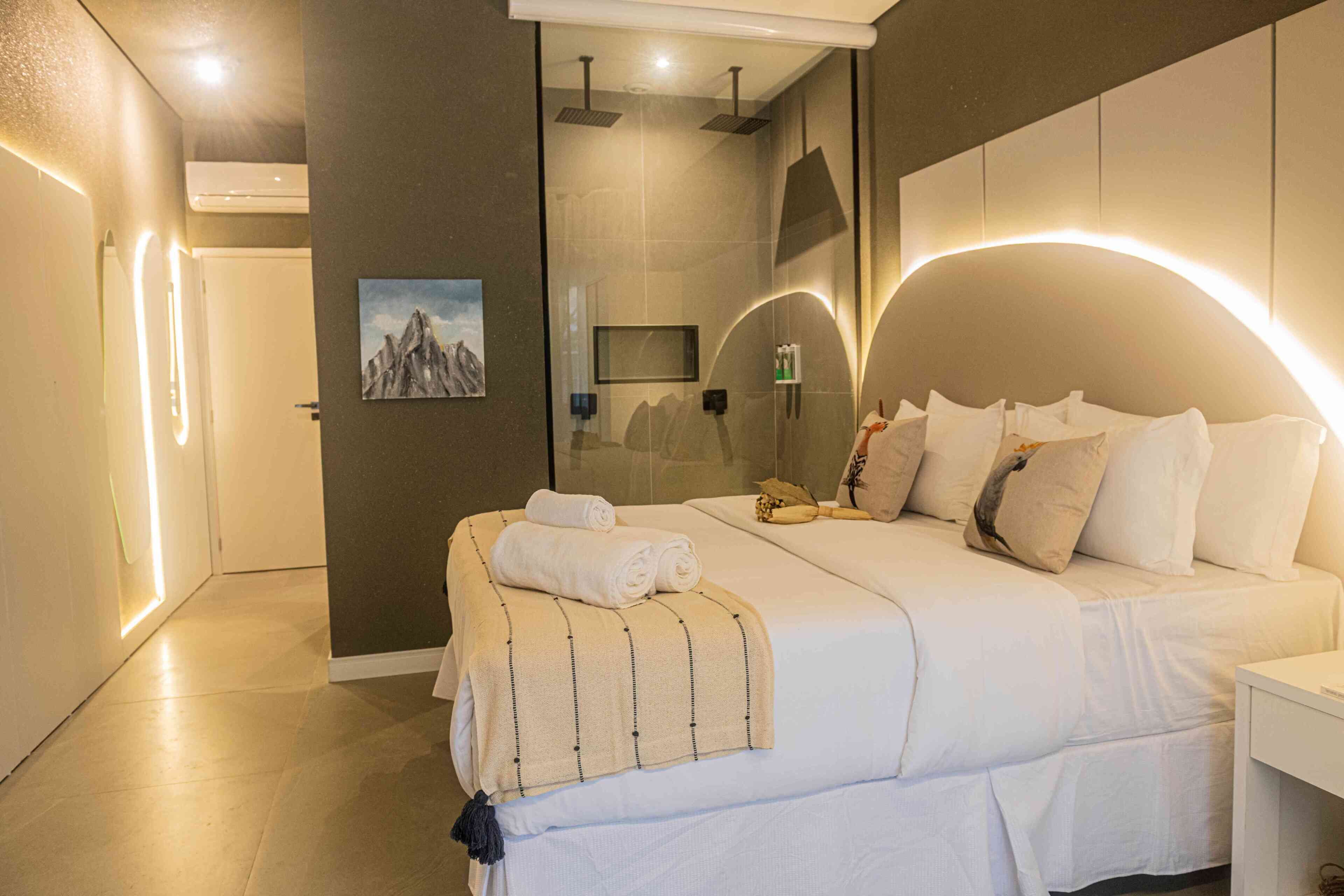Ein modernes Hotelzimmer mit einem großen Bett, einer Duschkabine und einem Wand-Fernseher.