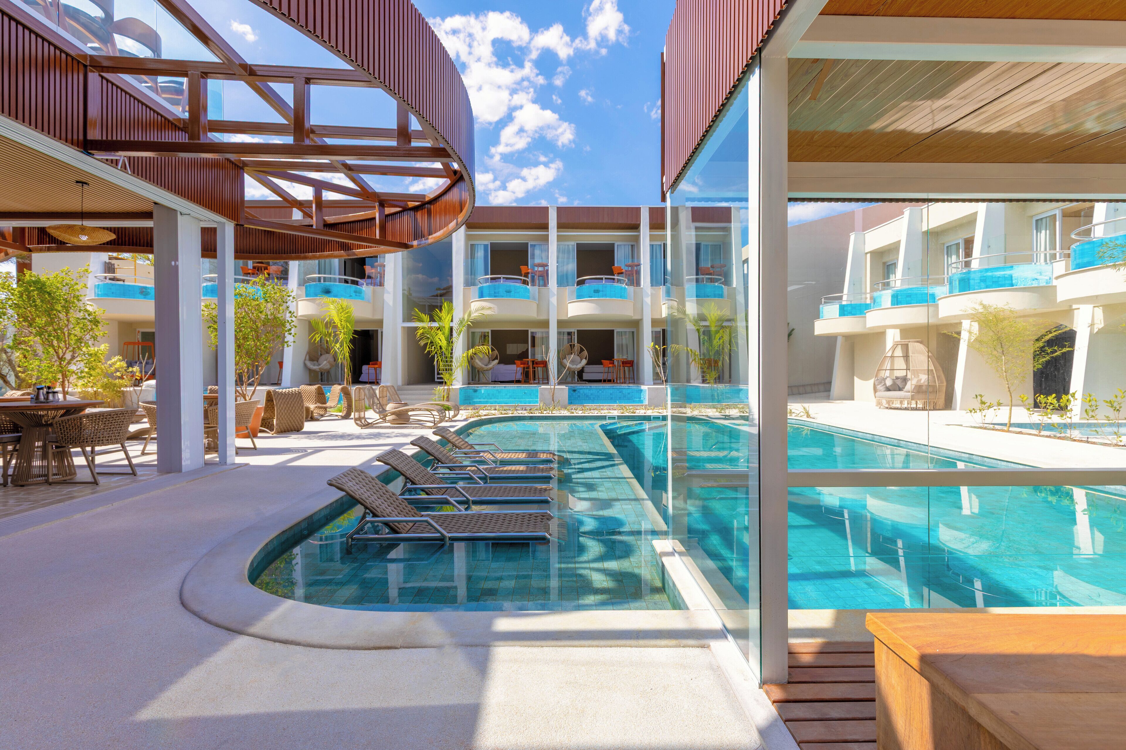 A modern hotel with a pool area, outdoor seating, and a clear view of the sky.