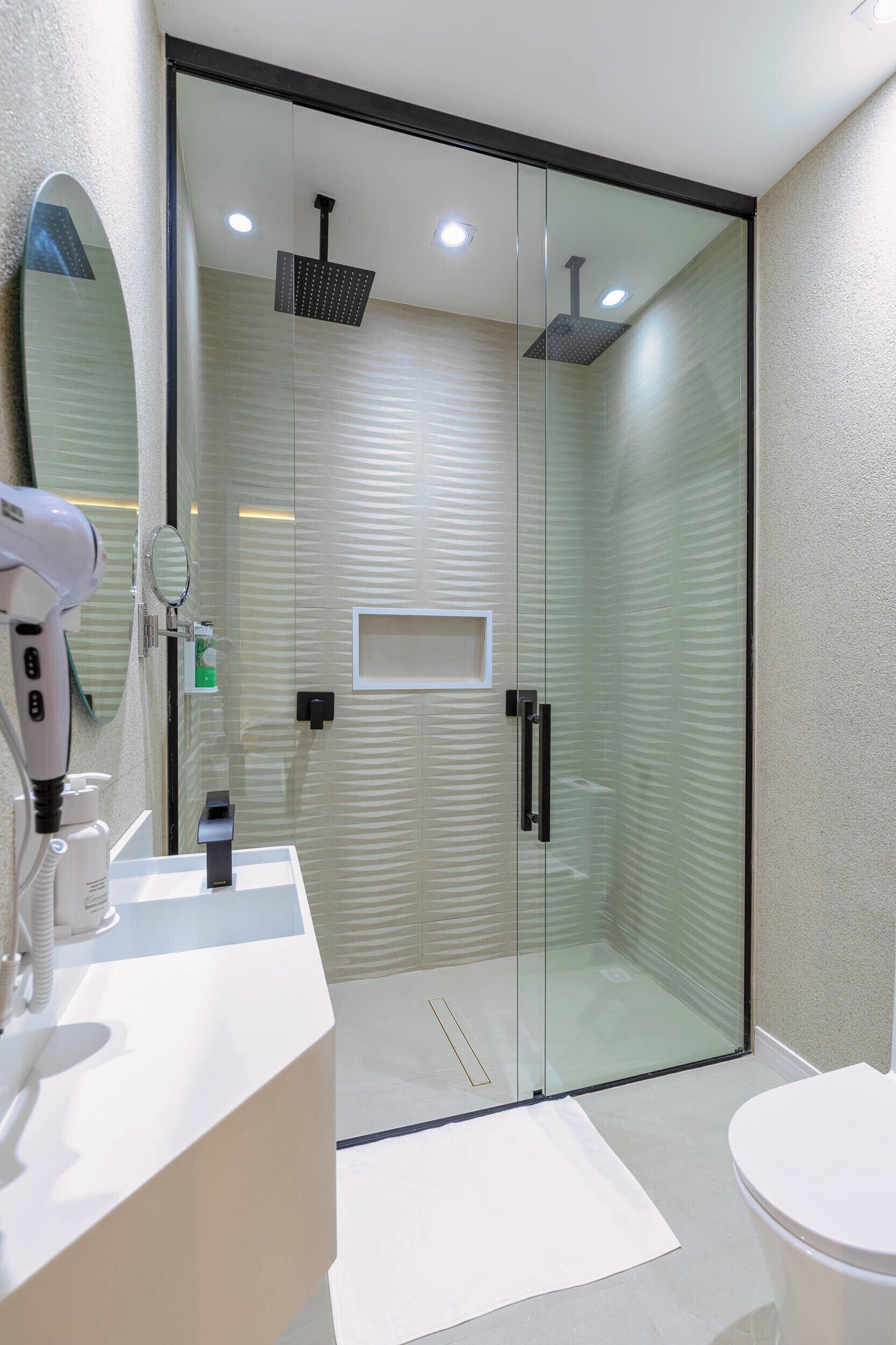 Un baño moderno con ducha de vidrio, un lavabo blanco y un secador de pelo, y un inodoro.