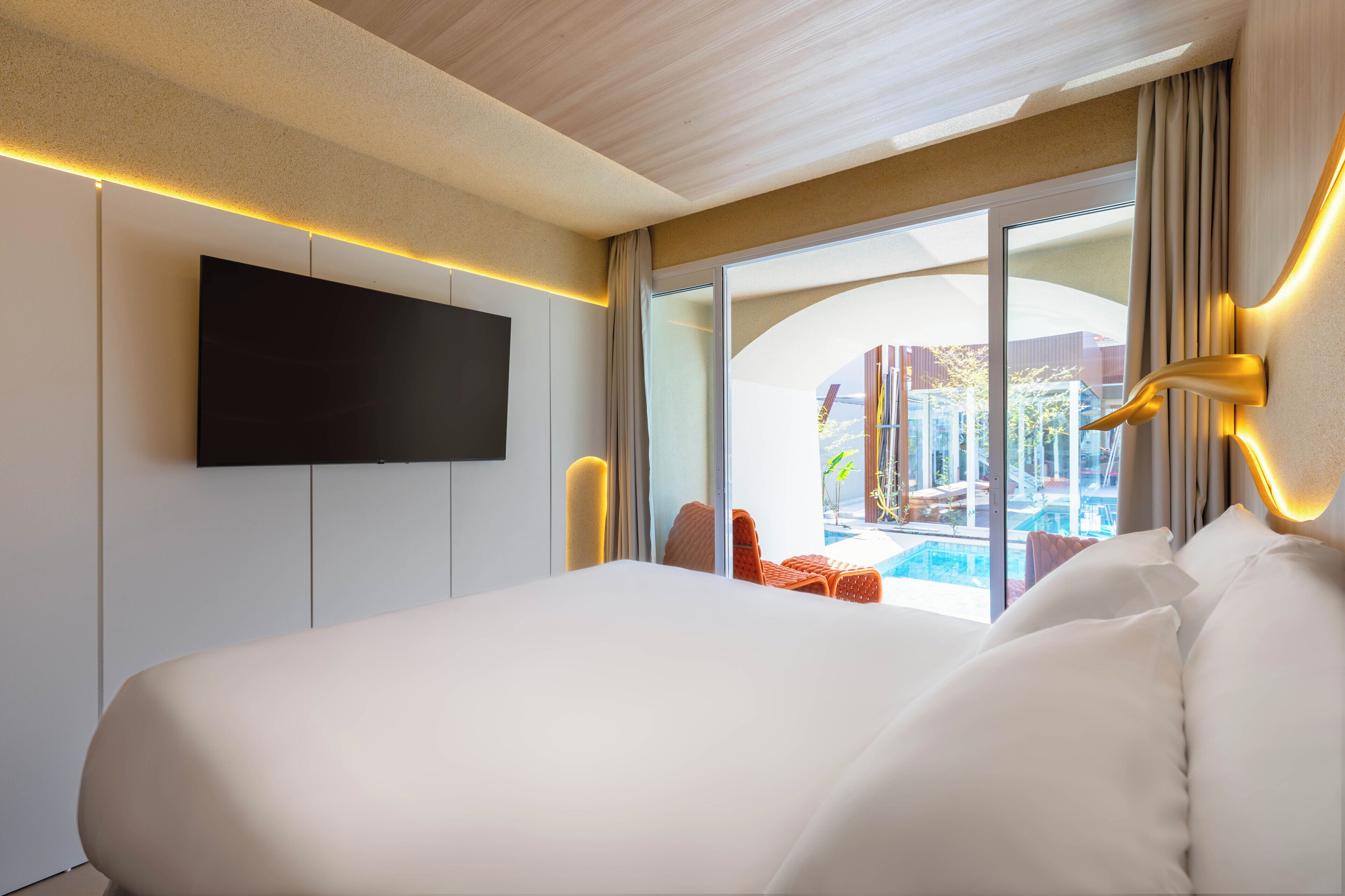 Ein modernes Hotelzimmer mit einem großen Bett, einem flachbildfernseher an der Wand und Blick auf einen Außenpoolbereich.
