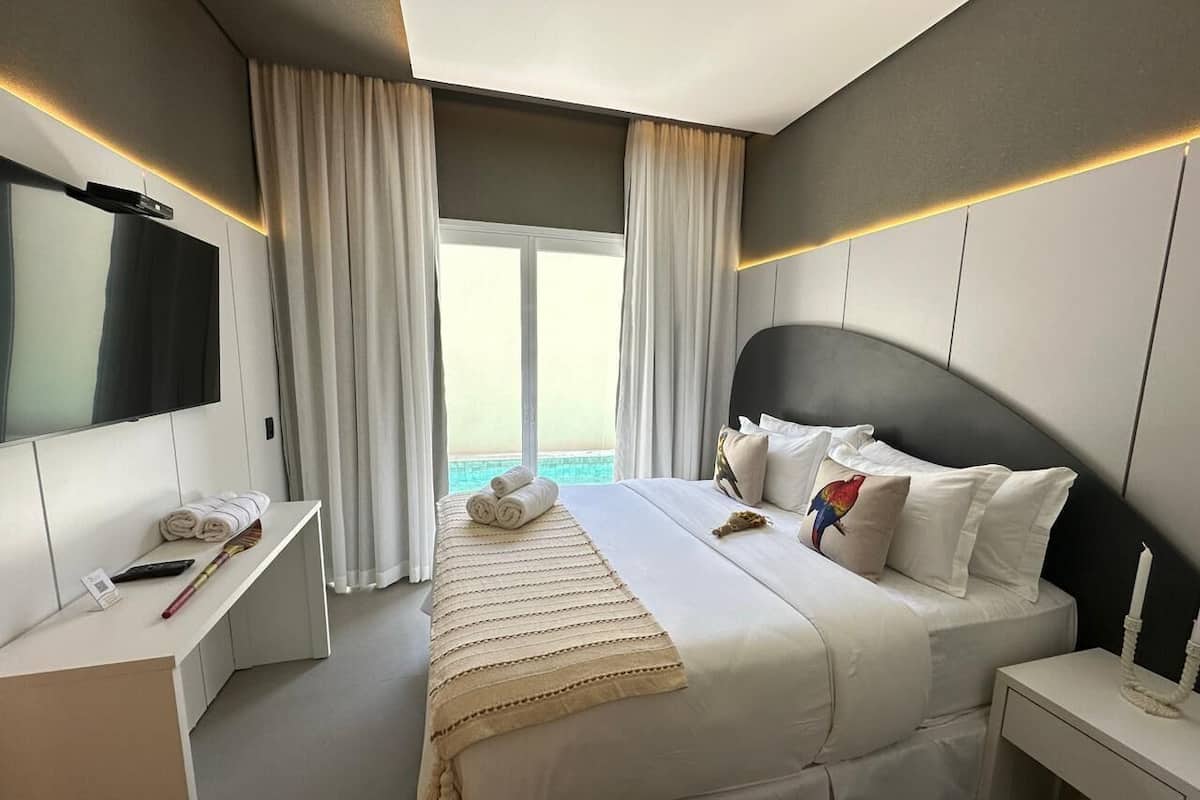 A modern hotel room with a large bed, a flat-screen TV, a desk, and a view of the sea.
