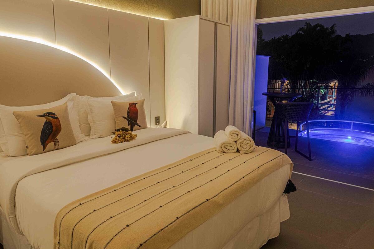 A hotel room with a large bed, a view of the outdoor area, and a balcony with a table and chairs.