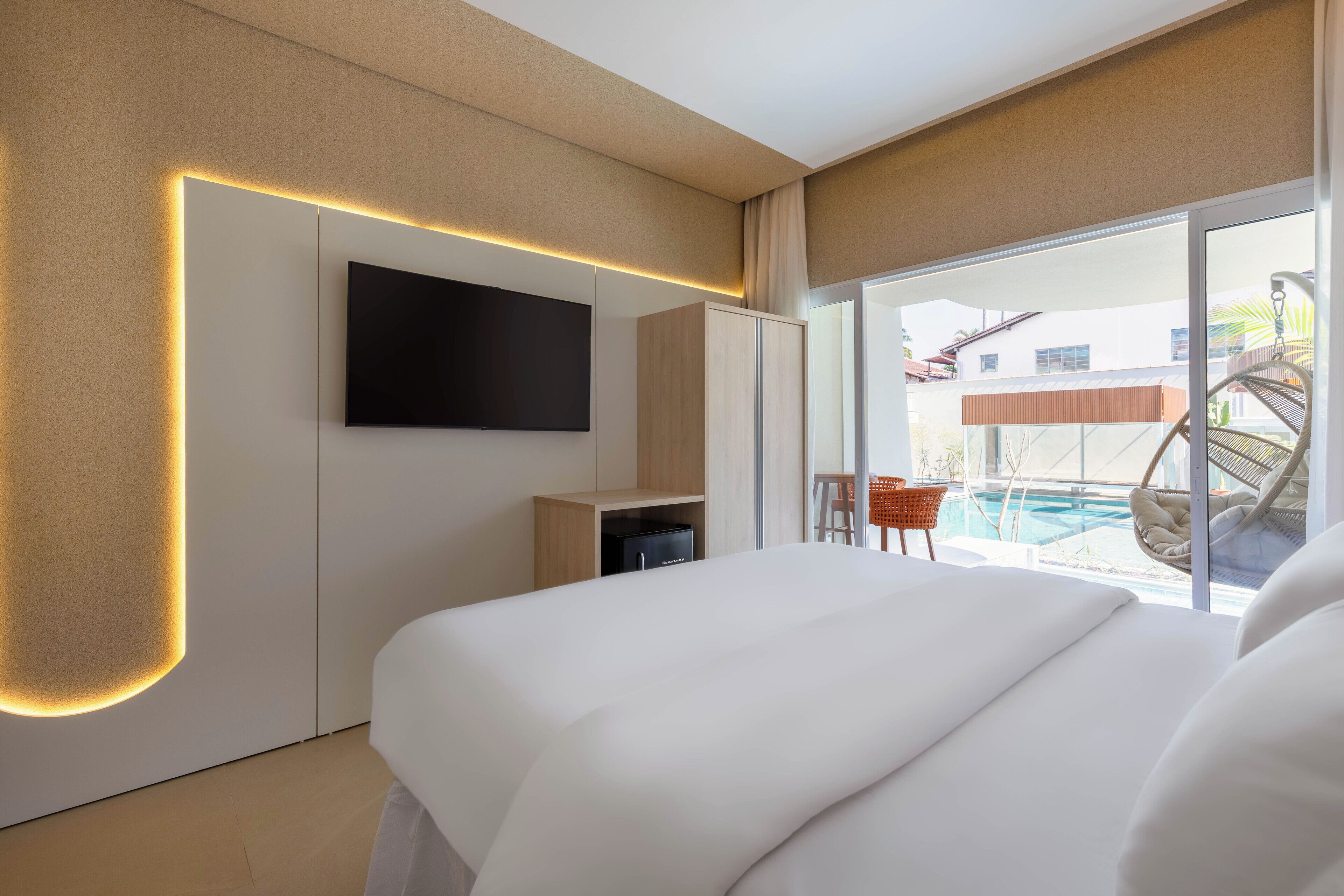 Ein modernes Hotelzimmer mit einem großen Bett, einem flachbildfernseher an der Wand, einem Kleiderschrank und Blick auf den Pool und den Außenbereich.