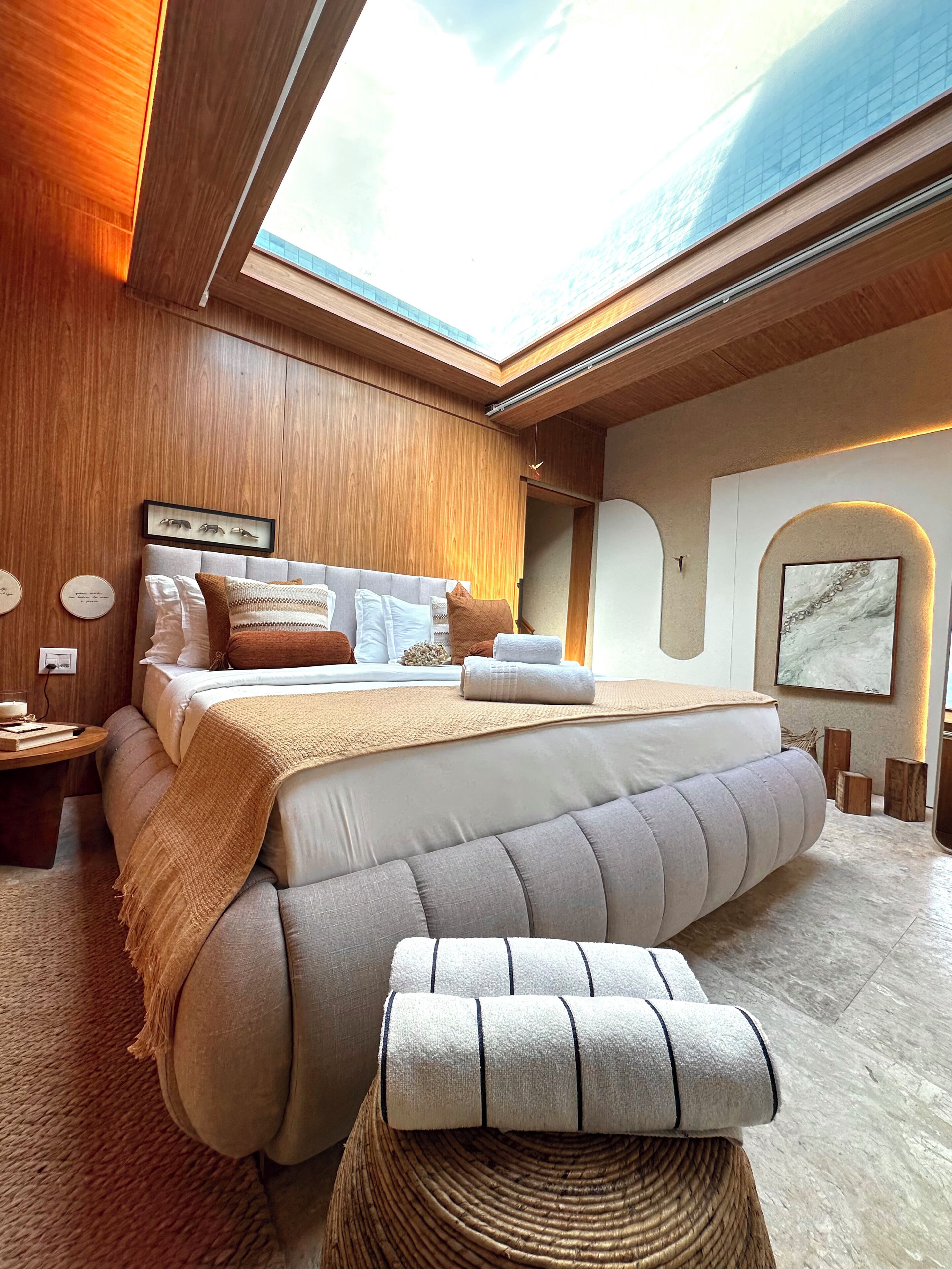A modern bedroom with a skylight, a large bed, a bedside table, and a wall-mounted artwork.
