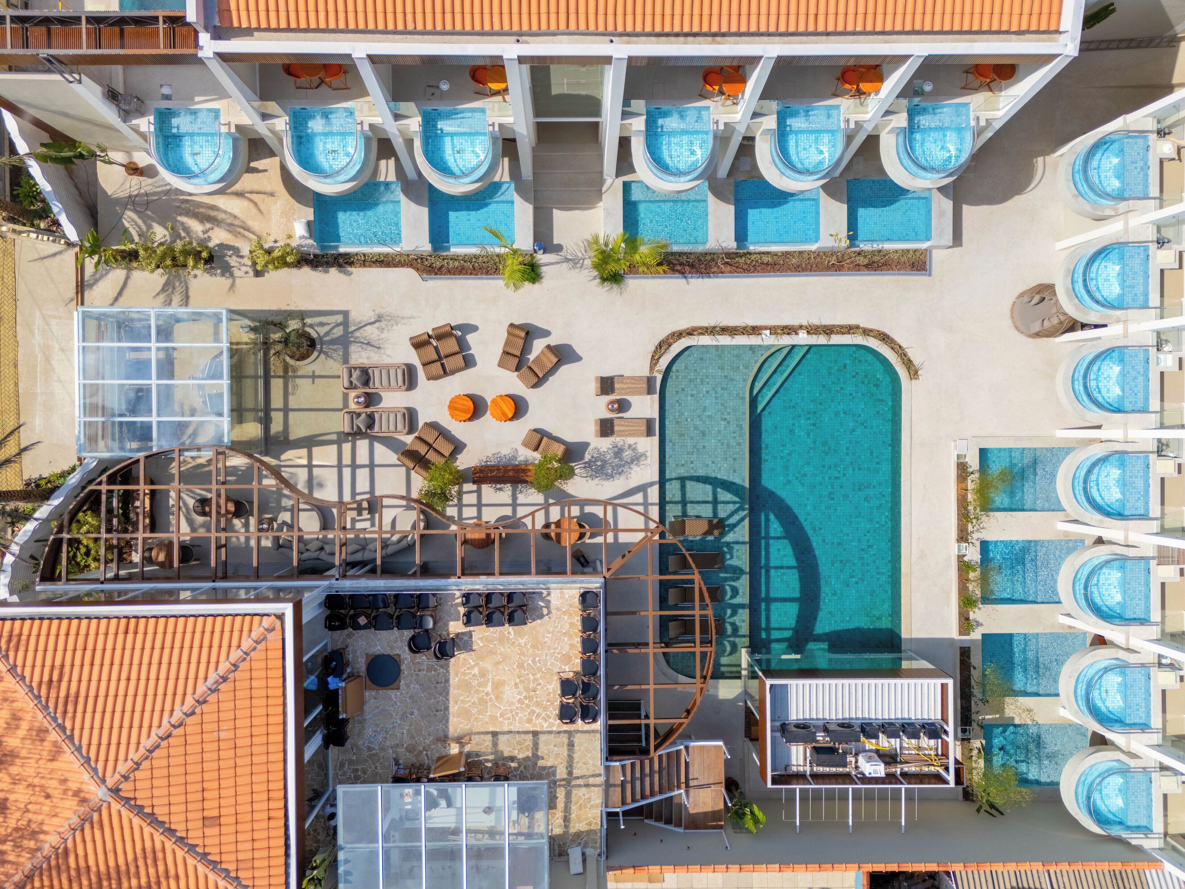 A rooftop pool area with multiple swimming pools, lounge chairs, and a central seating area.