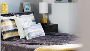 Un dormitorio con cama, mesita de noche, lámpara y dos cuadros.