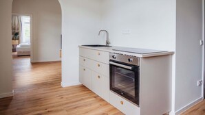 Une cuisine compacte avec des meubles blancs, un four encastré et un évier en acier inoxydable.