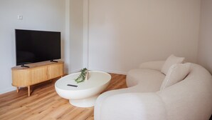 Un salon moderne avec un téléviseur à écran plat posé sur un meuble en bois, une table basse ronde blanche agrémentée d’une plante, et un canapé beige.
