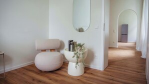 Une pièce moderne et minimaliste, avec une chaise ronde blanche, une petite table d’appoint blanche ornée de livres et d’une plante, et un grand miroir accroché au mur.