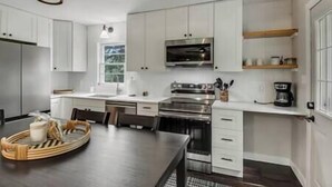A modern kitchen with white cabinets, a stainless steel oven, a microwave, and a coffee maker.