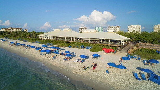 A beachside hotel with multiple blue umbrellas, a pool area, and a view of the ocean. - Spacious 3-bedroom condo minutes from beach with access to resort-like amenities (Naples)