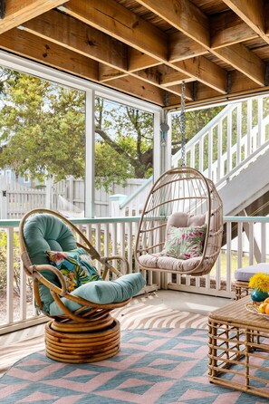 Un plafond en bois avec une balustrade blanche, une chaise en osier avec des coussins et une table en osier surmontée d’un tapis à motifs.