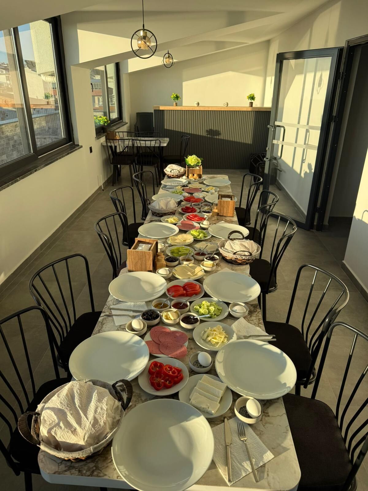 Un comedor con una larga mesa dispuesta para una comida, rodeada de sillas, y vistas a la ciudad a través de amplios ventanales.