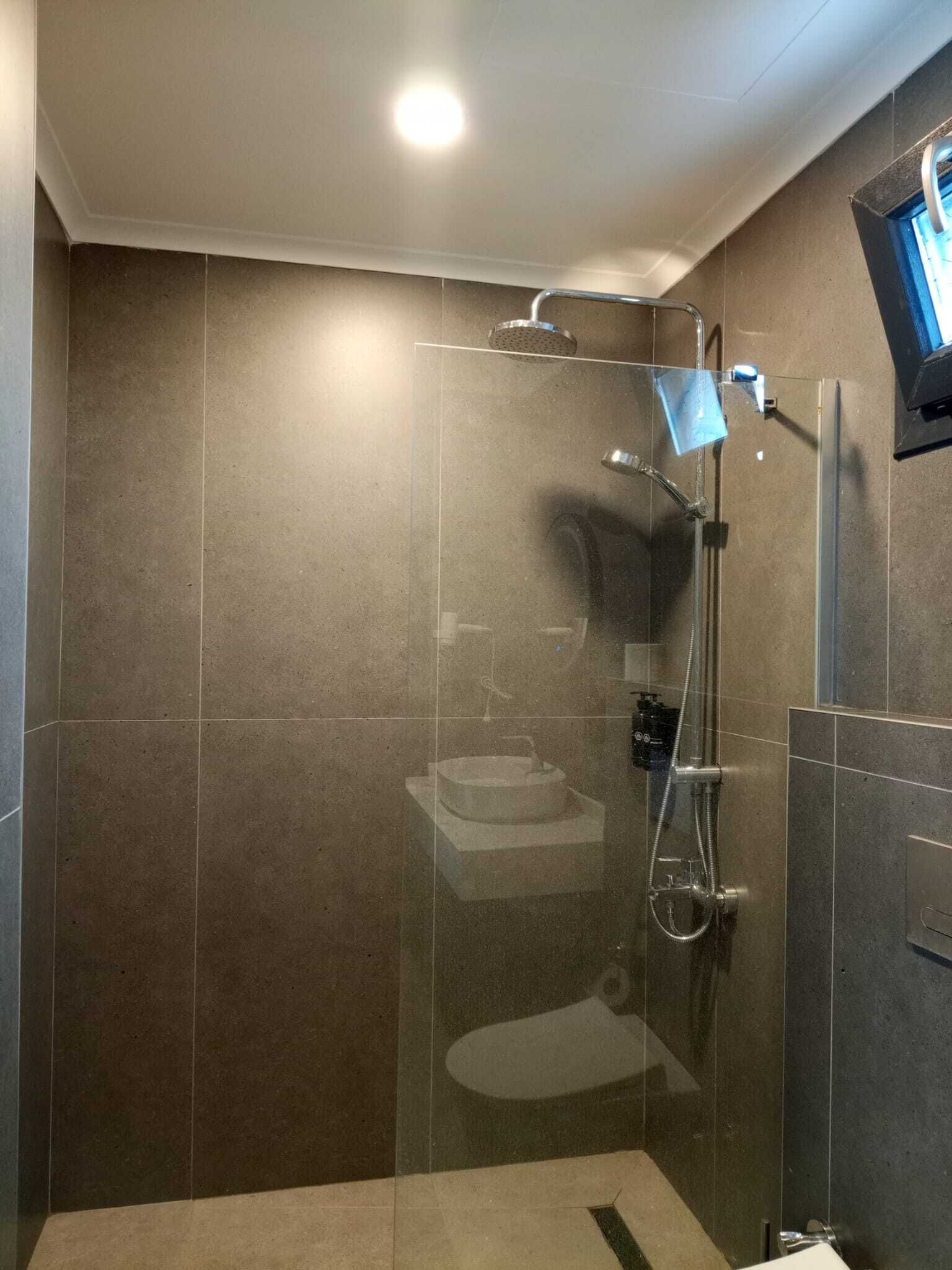 A modern shower with a glass door, a handheld showerhead, and a handheld shower attachment.
