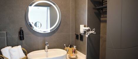 Un baño moderno con un espejo redondo, un lavamanos y un cesto para toallas.
