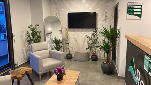 A modern hotel lobby with a reception desk, a seating area with a sofa and coffee table, and several potted plants. - Koç Guest House (Demirkoy)